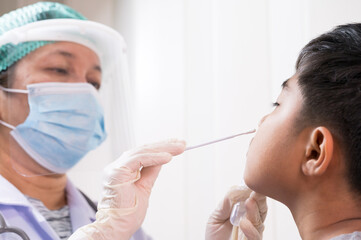 Naklejka premium Doctor taking a swab for corona virus sample from potentially infected Asian boy nose.Covid-19 laboratory test.Medical staff with PPE suit test covid-19 to asian kid by nose swab at hospital.