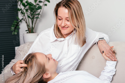 Blonde mom and teen daughter talking at home on the couch.The daughter is lying on her mother's lap.Time together,women's generation, International Women's Day, Happy Mother's Day.