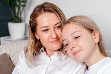 A mother and her teenage daughter are sitting on the couch at home, hugging each other and spending time together. Women's generation, International Women's Day, Happy Mother's Day.