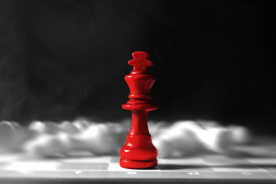Red chess piece among ordinary ones on checkerboard against dark background