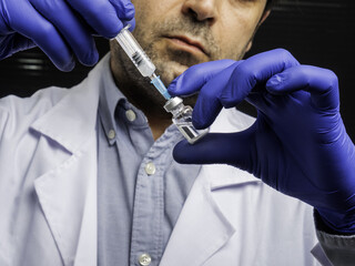 Caucasian doctor wearing gloves obtaining vaccine from a vial using a syringe