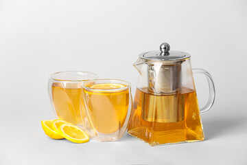 Teapot with hot tea, glasses and lemon on light background