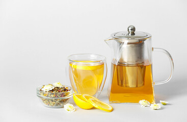 Teapot with hot tea, dry leaves and lemon on light background