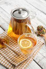 Teapot with hot tea and honey on light wooden background