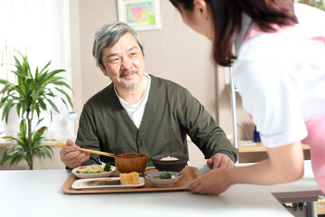 食事を運ぶ女性介護士と高齢者の白髪男性