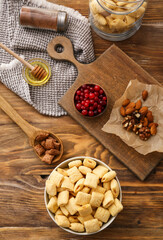 Bowl with tasty corn pillows, cranberries and nuts on wooden background