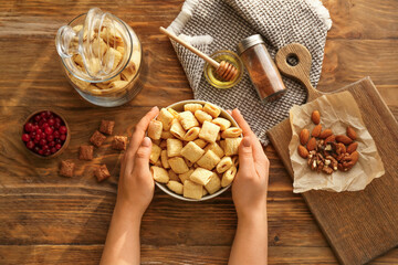 Female hands and bowl with tasty corn pillows on wooden background