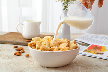 Woman pouring milk into bowl with tasty corn pillows on light background