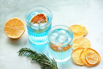 Glasses of cocktails with ice and dried citrus fruit on light background