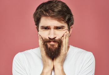 Guy touches his face with his hands on a pink background cropped view