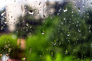 Rain droplets on a window glass pane with green trees on the background. Selective focus.