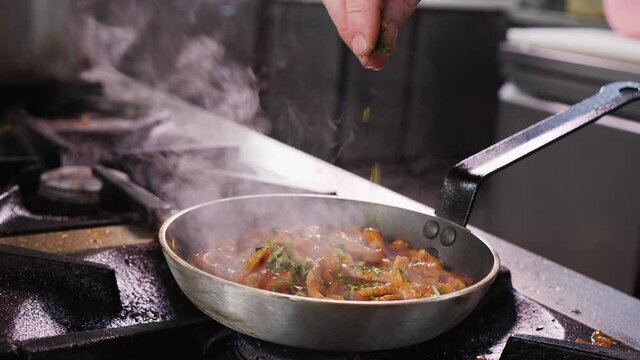 Making fried pork Brasso style - cooking the pork meat strips with the vegetable sauce, sprinkle with green parsley leaves, close up, camera slow orbit