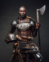 Wild barbaric person with black skin wielding an axe posing in dark background