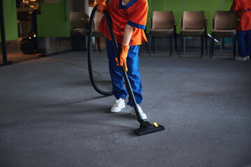 Female janitor vacuuming the carpeted floor in the conference hall
