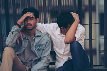 Sad Depressed two Insomnia Men. Sitting on the street sidewalk after lost job. Young jobless man suffering depression sitting on ground street underground leaning on high steel cage fence