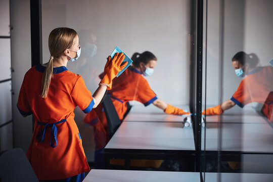 Two cleaning ladies in face masks sanitizing office surfaces