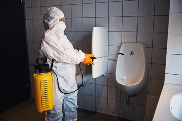 Trained cleaner in rubber gloves sanitizing the urinal