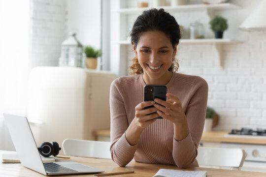 Overjoyed Millennial Hispanic Female Remote Student Learn From Home Take Break In Study To Read Good News At Chat On Cell Screen. Happy Young Latin Lady Relax From Distant Work Hold Phone Text Message