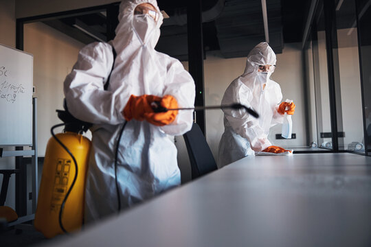 Two qualified cleaners in hazmat suits sanitizing hard surfaces