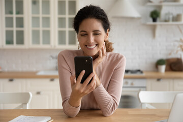 In a good mood. Smiling young hispanic lady sit at kitchen table enjoy talk by video call dating on...