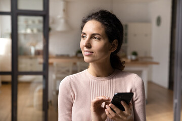 Calm young hispanic woman use mobile phone look aside distracted from gadget think on information received from web. Millennial female hold cell look at distance before write answer on text message