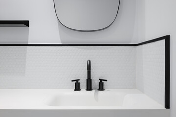 White honeycomb tile bathroom with wash basin, mirror and black faucet.