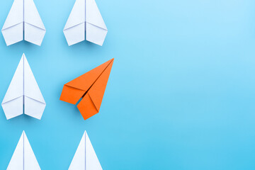 Business concept for new ideas creativity and innovative solution, Group of white paper plane in one direction and one orange paper plane pointing in different way on blue background - obrazy, fototapety, plakaty