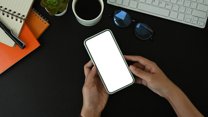 Top view of woman holding mobile phone with blank screen on black leather.