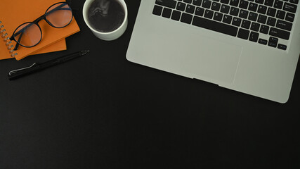 Modern dark office desk with laptop computer, coffee cup, glasses and copy space on black leather.