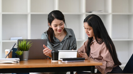 Two young businesswoman using digital tablet and discussing new startup project in modern office.