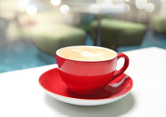 Red coffee mug on table blurred cafe background. Cup of cappucino or latte closeup.