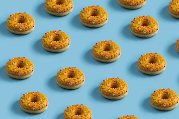 Creative pattern donut design, many donuts decorated with yellow glaze and a multi-colored sprinkle on blue background