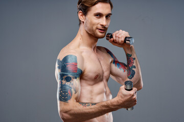 Fototapeta na wymiar male athlete with a tattoo on his arm naked torso inflated muscles dumbbells fitness