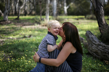 Fototapeta premium Mother and son snuggling in field full of spring wildflowers