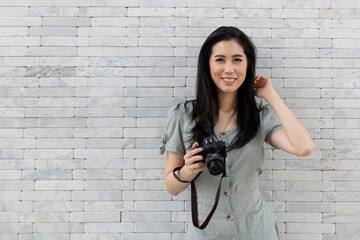 Portrait of a happy Asian girl in dress standing by the stone wall. Young traveling woman standing near stone wall during holiday. Tourist woman standing by the wall.