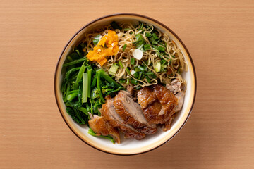 Dry roast duck noodles in a ceramic bowl on wooden table. Top view.