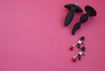 Toys for sex. Nipple clamps and anal dildos on a pink background.