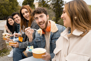 Young people with face mask on the wrist having fun eating take away food at the park using...