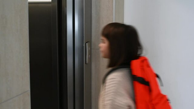 girl child schoolgirl 8 years old with an orange backpack goes into the elevator at home. High quality 4k footage