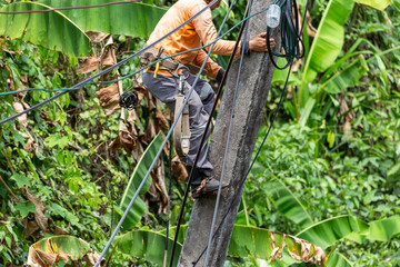 Electrician workers with tools for cutting and connecting wires Climb the electric pole, tilt it, repair the broken wires. It's a very risky job. The electric pole tilts, causing a summer storm.