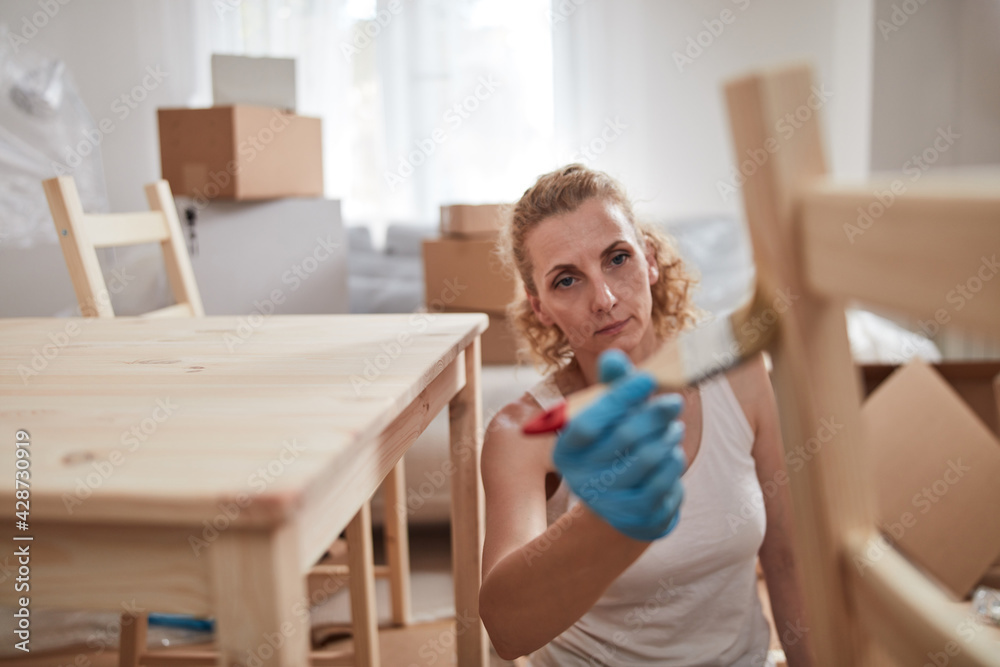 Wall mural Woman painting and assembling furniture in new apartment, moving in and being hardworking.