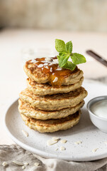 Stack of vegetarian oatmeal pancakes for breakfast decorated with nuts, jam and mint, light stone background.