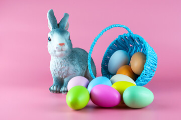 a rabbit and an overturned basket with colorful Easter eggs on a pink background