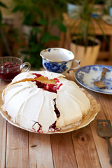 Pavlova cake with vanilla cream and cherry sauce. Side view. Wooden background and green plants.