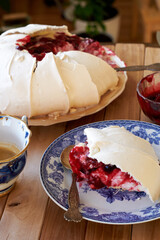 Pavlova cake with vanilla cream and cherry sauce. Side view. Wooden background and green plants.
