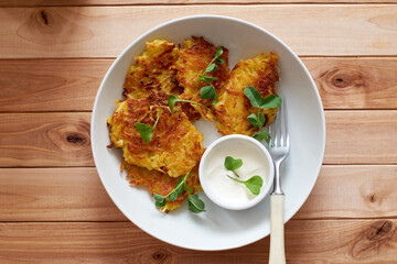 Potato pancakes or pancakes with sour cream in a plate on a wooden background. Top view.