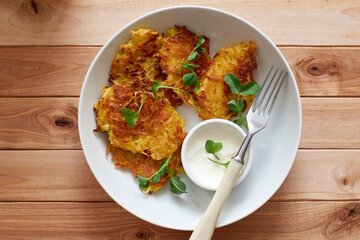 Potato pancakes or pancakes with sour cream in a plate on a wooden background. Top view.