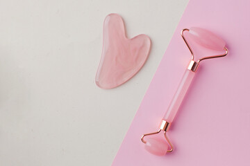 Flat lay rose quartz gua sha stone, jade roller on a light background. The concept of home skin...