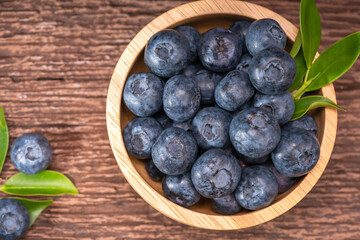 Fresh Blueberries on wooden tray with green leaves background.