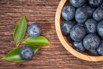 Fresh Blueberries on wooden tray with green leaves background.
